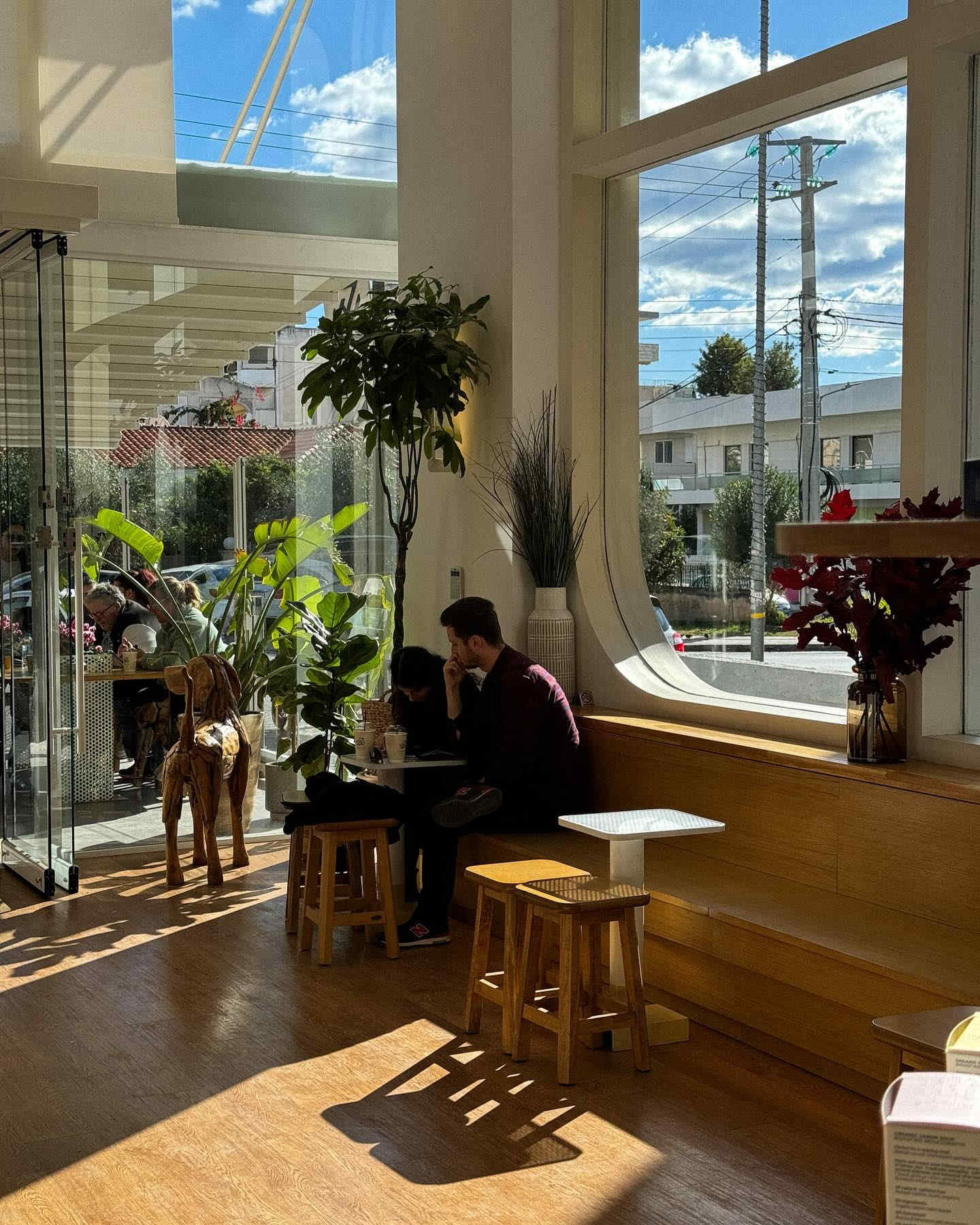 φωτογραφία από το καφέ Keziah Espresso Bar στη Γλυφάδα, όπου ένας πελάτης εργάζεται σε φορητό υπολογιστή δίπλα σε ένα μεγάλο παράθυρο