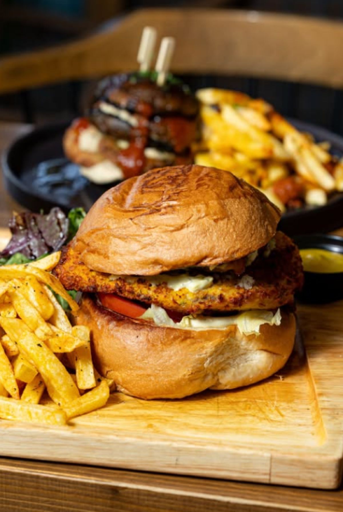 Ένα τεράστιο burger με ζουμερό μπιφτέκι, λιωμένο τσένταρ, πίκλες και καραμελωμένα κρεμμύδια, σερβιρισμένο σε ξύλινη επιφάνεια