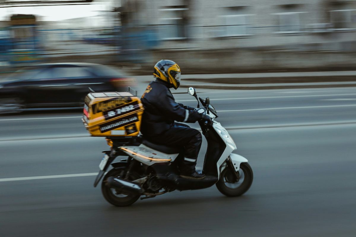 Διανομέας φαγητού οδηγεί τη μηχανή του μέσα στην κίνηση της πόλης κατά τη διάρκεια της εργασίας του