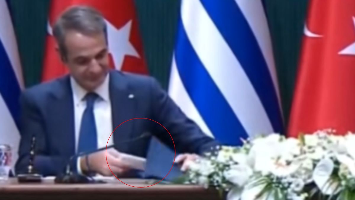 Κοντινή λήψη στα χέρια του Πρωθυπουργού που τοποθετούν έναν φάκελο πάνω από ένα χαρτομάντιλο πάνω στο τραπέζι