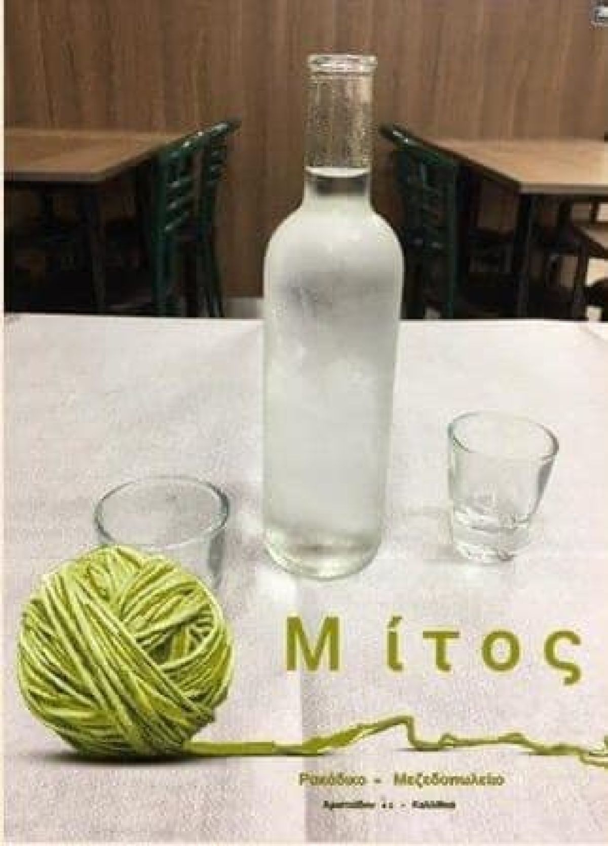 Ένα κρυστάλλινο καραφάκι με παγωμένη ρακή και μικρά ποτηράκια πάνω σε ένα τραπέζι, έτοιμα για πρόποση σε κρητικό ρακάδικο
