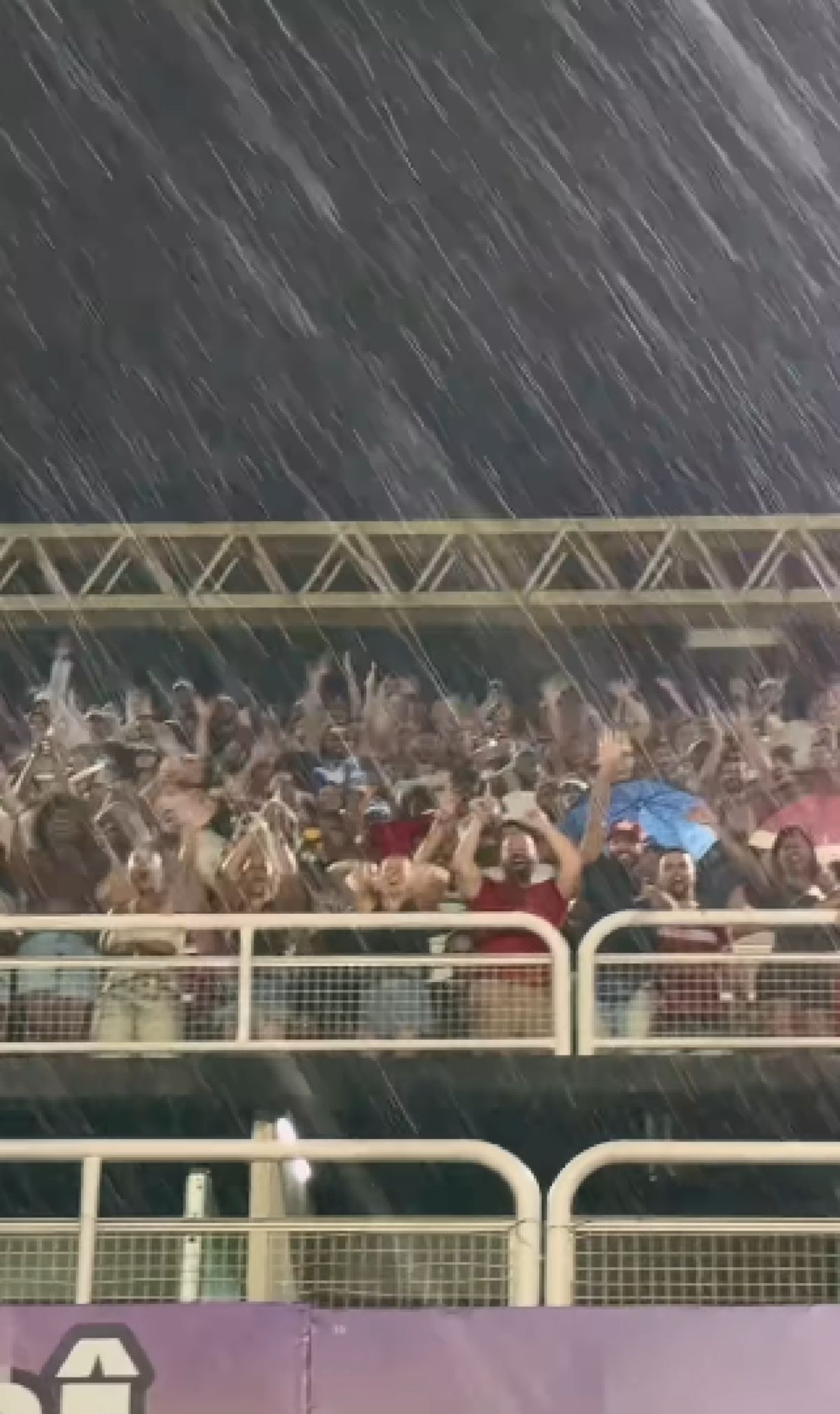 Κατάμεστες κερκίδες του Sambadrome στο Ρίο, με κόσμο να κρατά πλακάτ και να ζητωκραυγάζει υπό τη βροχή, υποστηρίζοντας την κοινότητα του Σάο Γκονσάλο