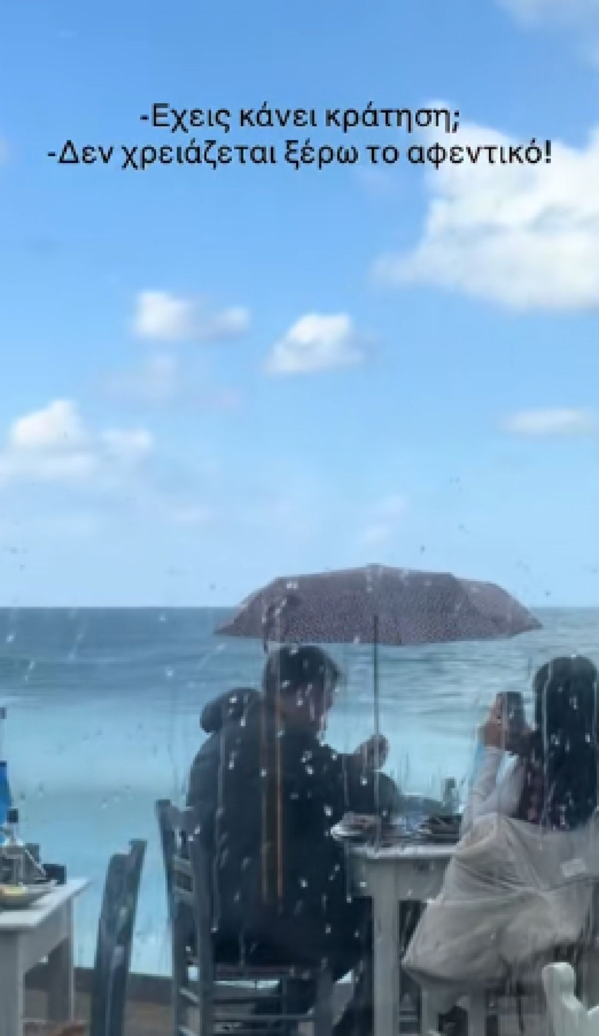 Στιγμιότυπο από εστιατόριο όπου πελάτες τρώνε στη βροχή κρατώντας ομπρέλα δίπλα στο κύμα